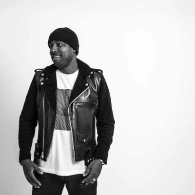 Man wearing a black beanie, leather vest, and smiling.