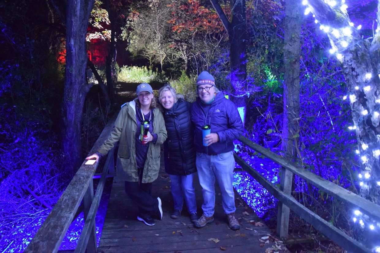 Three people on a lighted bridge at night.