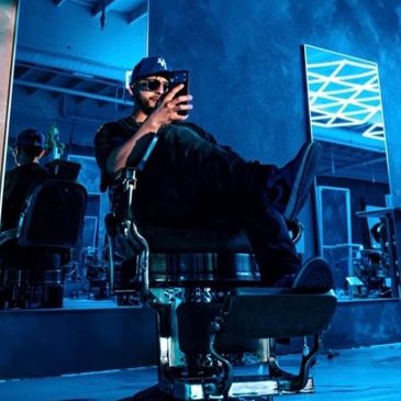 Man sitting on a barber chair taking a selfie.