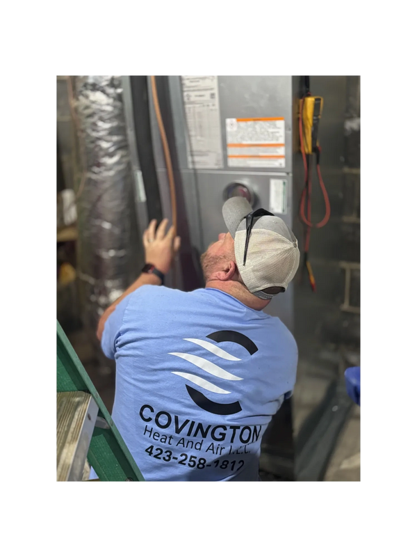 Technician in Covington Heat and Air shirt servicing HVAC unit.