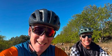 Two men smiling outdoors with helmets and sunglasses.