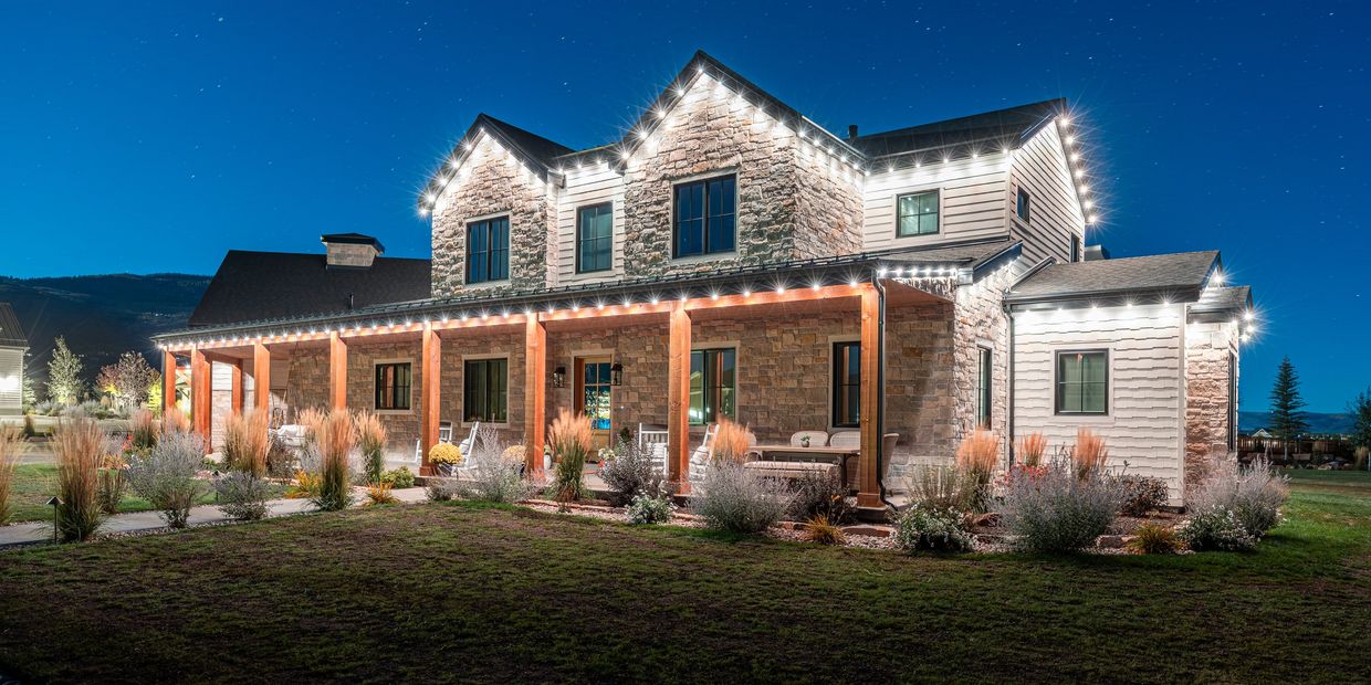 A beautifully lit stone house with a spacious porch at night under a starry sky.