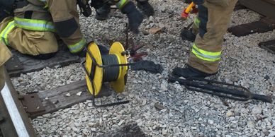 Firefighters work on a rocky railway track with equipment.