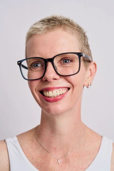 Smiling woman with short blonde hair and black glasses.
