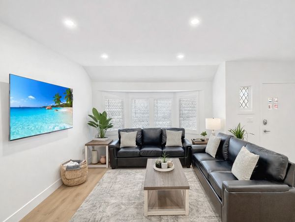Modern living room with black leather sofas, wooden coffee table, and a wall-mounted TV.