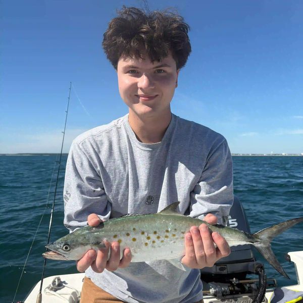 Teen boy proudly holds a large Spanish Mackerel while on a boat in the ocean. 