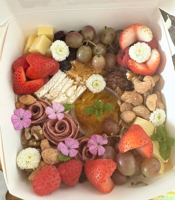 A colorful charcuterie box with fruits, nuts, cheese, and flowers.