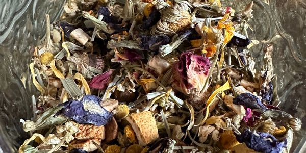 A mix of dried flowers and herbs in a glass container.