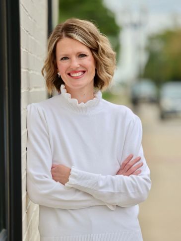 Smiling woman in white sweater leaning on a wall.