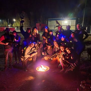 Group of friends posing with toy guns around a campfire at night.