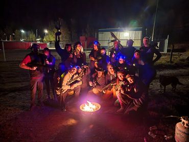 Group of people with laser tag gear around a campfire at night.