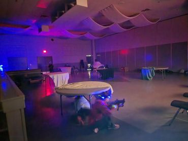 People playing laser tag in a dimly lit indoor arena with tables.