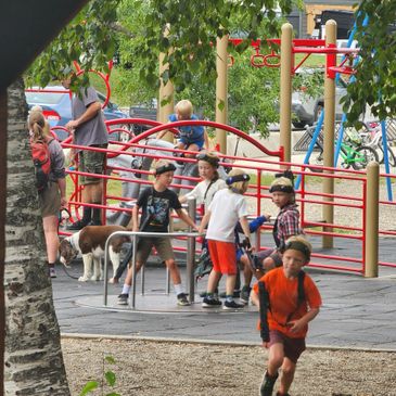 Children playing energetically on playground equipment surrounded by trees and adults.
