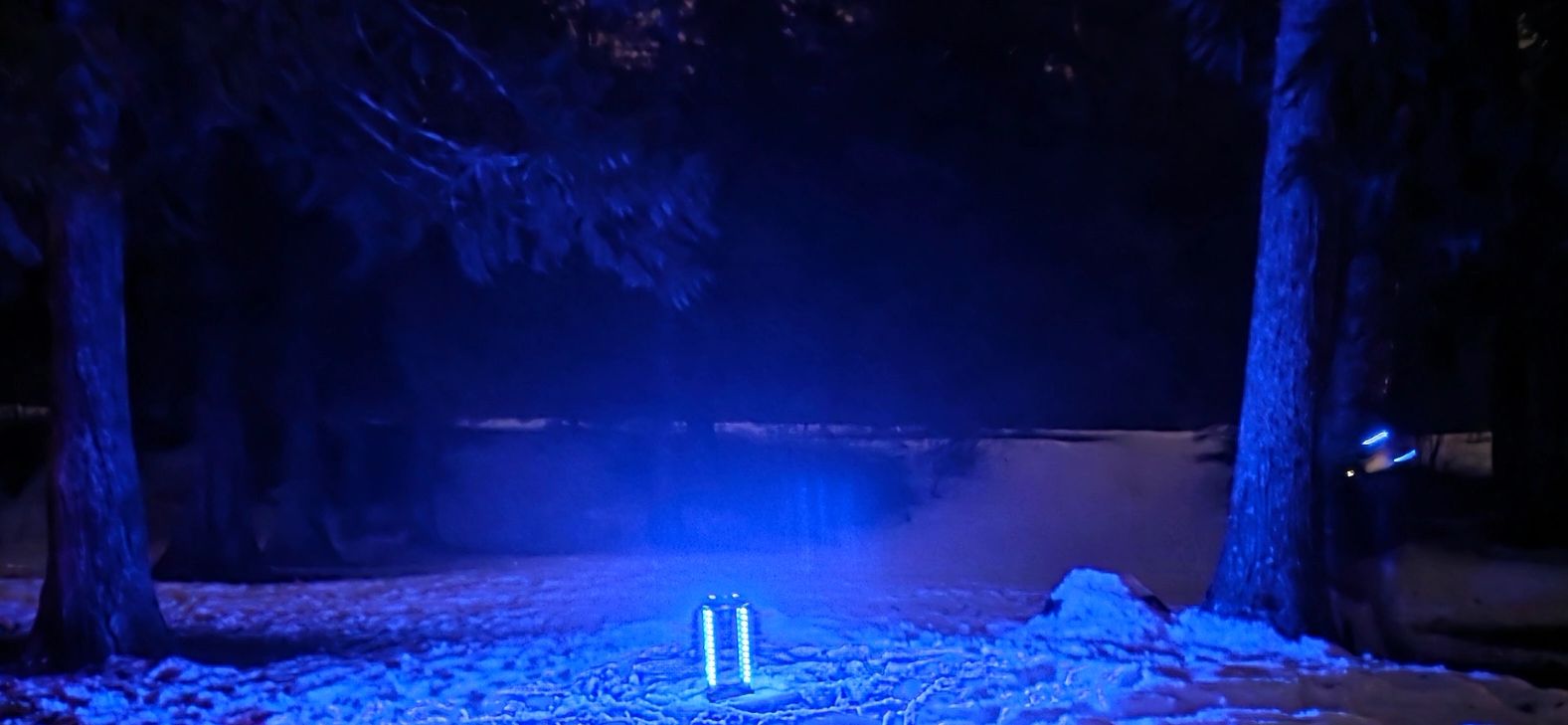 Blue glowing light (Base) illuminates snowy ground in a dark forest at night, flanked by lasertag players.