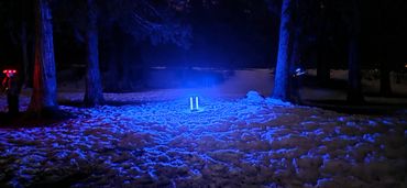 A glowing blue light illuminating snow and trees at night.