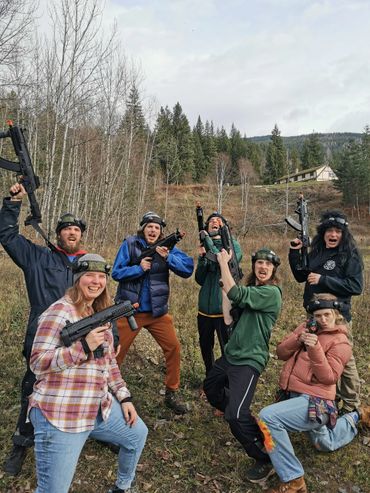 Group of seven people outdoors holding paintball guns and posing excitedly.