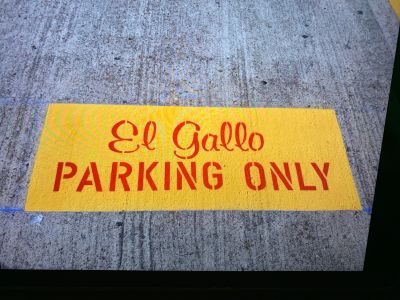 Yellow parking sign on concrete: 'El Gallo PARKING ONLY'.