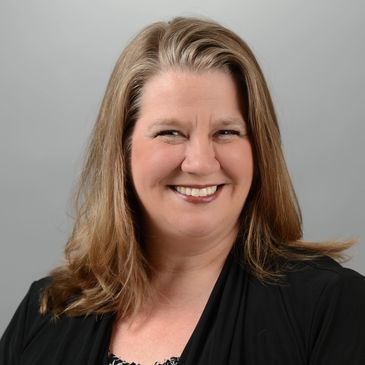 Smiling woman with long hair against a gray background.