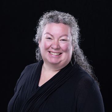 Smiling woman with curly gray hair against a black background.