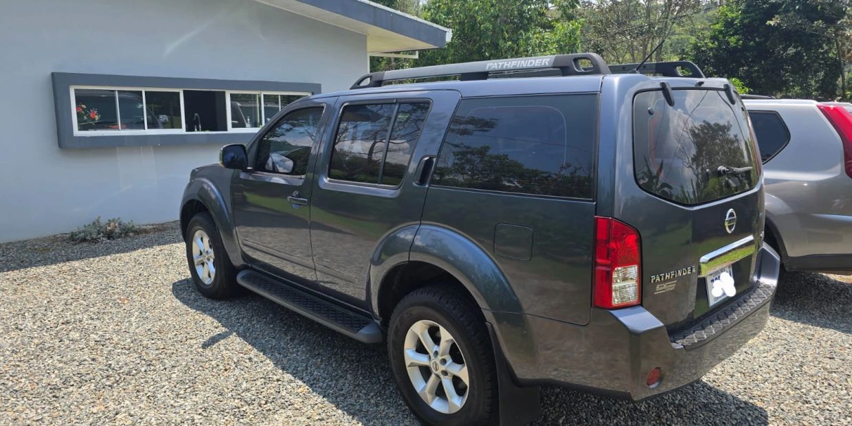 Dark gray Nissan Pathfinder parked on gravel near a light blue building.
