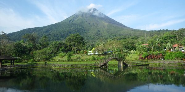 A serene lake reflecting a lush green mountain with a cloudy peak.
