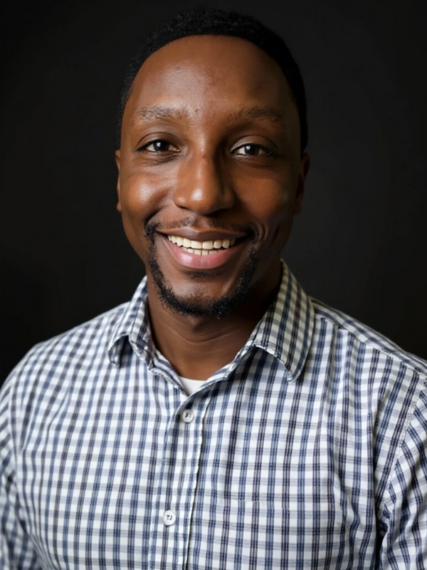 Smiling man in a checkered shirt against a black background.
