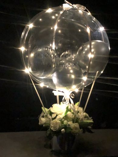 Flower arrangement in hat box with clear balloon on top designed to look like a hot air balloon 