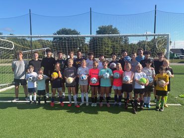 Youth soccer team posing with soccer balls on field.