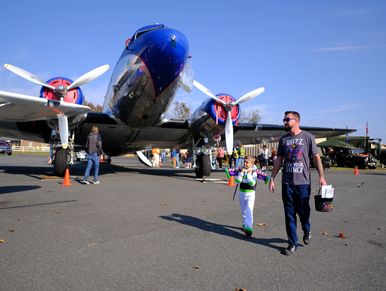 A man and child walk near a vintage airplane on a sunny day.