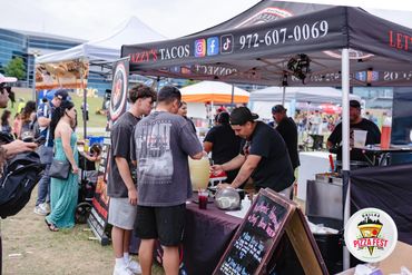 People ordering food at a taco stand during an outdoor festival.