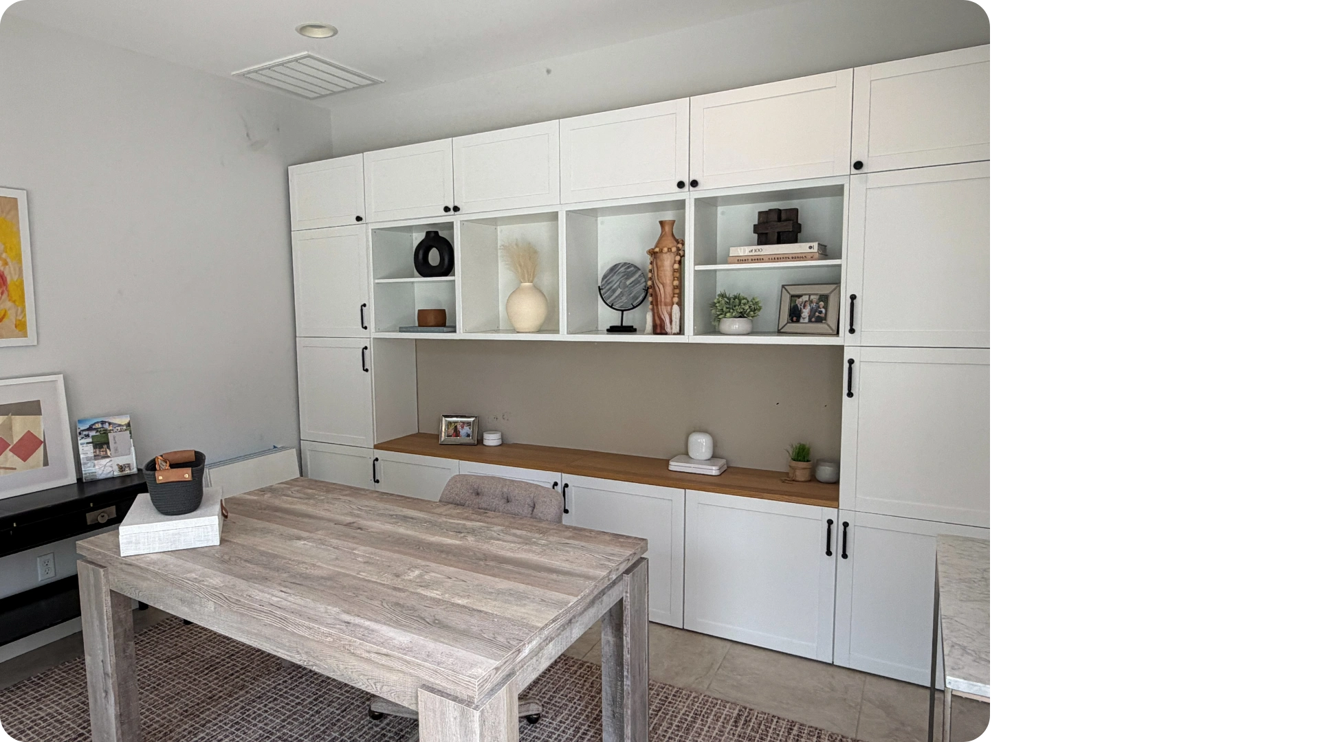 Modern office with white cabinets, wooden desk, and decorative items on shelves.