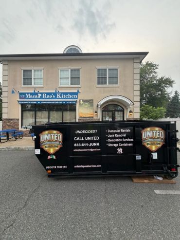 Black dumpster with United Junk Services logo in front of Mama Rao's Kitchen.