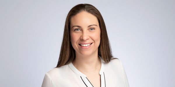 Smiling woman with long brown hair in a white blouse.