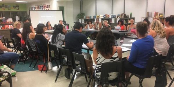 A group meeting in a library, seated in a circle for discussion.