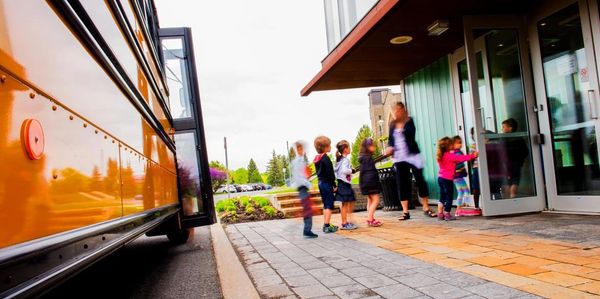 Des enfants entrant dans une école après un trajet en bus scolaire.