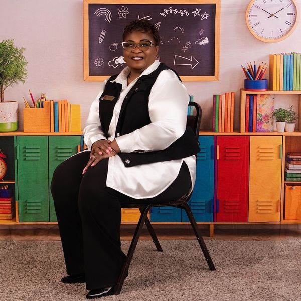 Confident teacher seated in colorful classroom with educational decor.