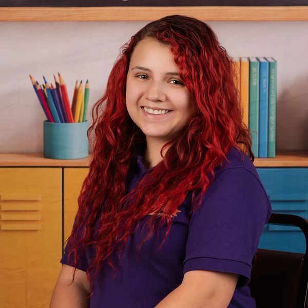 Young woman with vibrant red hair smiling indoors in a colorful room.