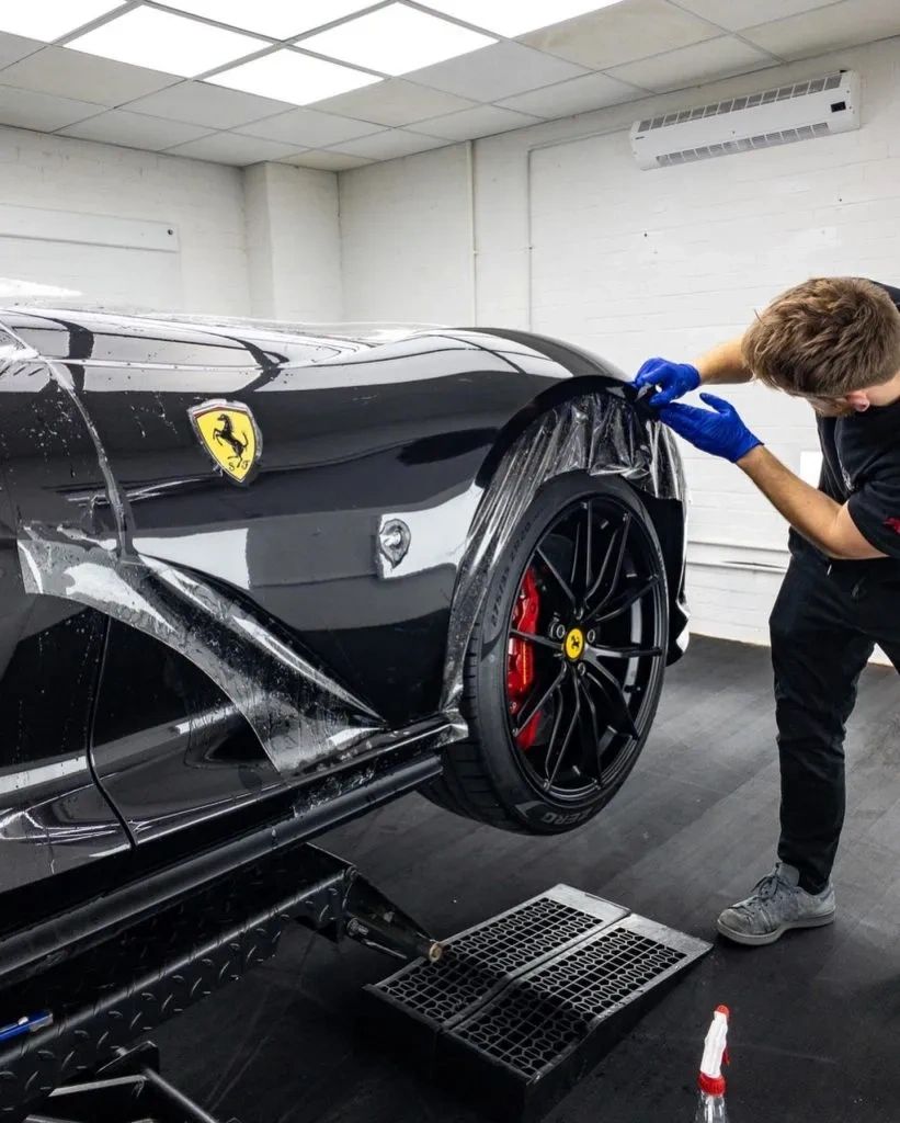 A person applying protective film on a black Ferrari's front fender.