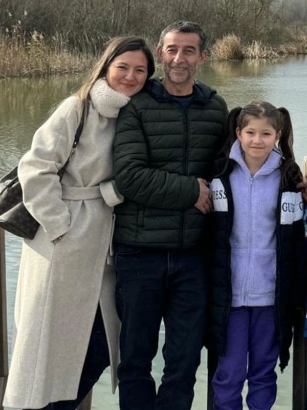 A happy family of three posing near a lake on a chilly day.