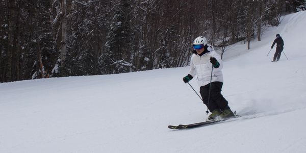 Two people skiing on a snowy slope surrounded by trees.
