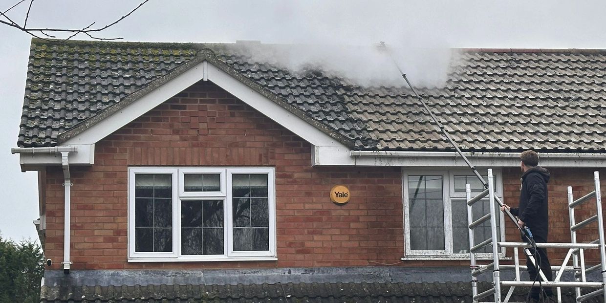 Person cleaning moss off a tiled roof using a pressure washer.