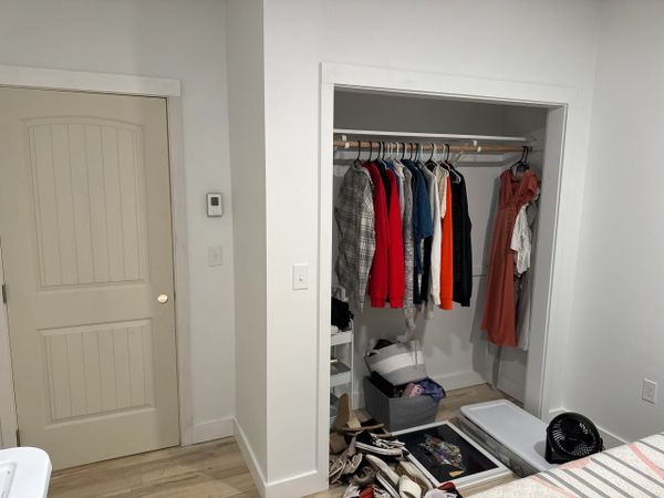 Open closet with clothes hanging and items on the floor in a minimalistic room.