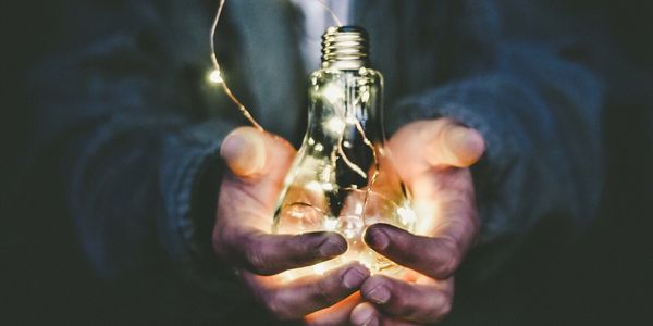 Hands holding a glowing light bulb.