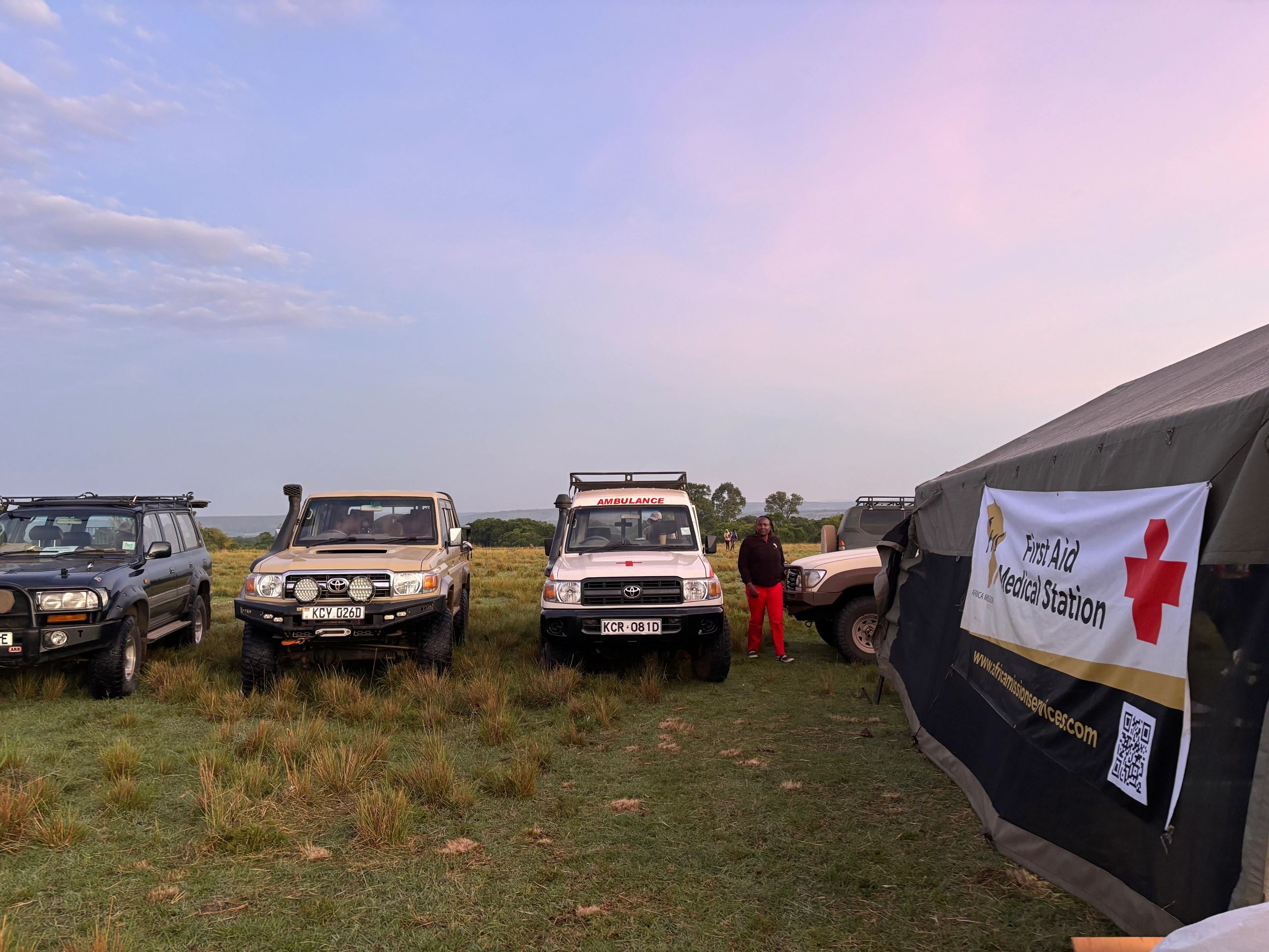 Safari vehicles and a first aid tent in a grassy area.
