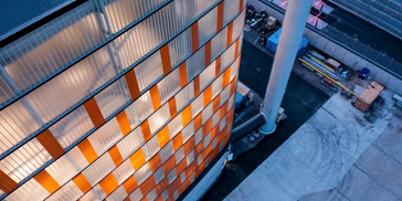 Aerial view of a modern building with illuminated windows and surrounding industrial area.