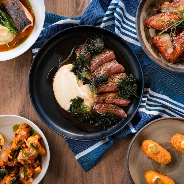 A gourmet meal featuring steak, salmon, wings, and croquettes on a wooden table.