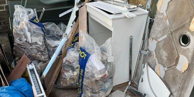Renovation debris and discarded furniture piled on a wooden deck outside a brick building.