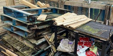 Stacked wooden pallets and scattered garden supplies in a backyard.