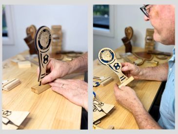 A person assembling a wooden soccer trophy model on a table.