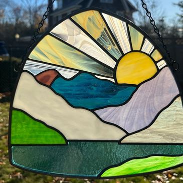 Image of a stained glass panel in the shape of a shield, with crisp blue water, various color mounta